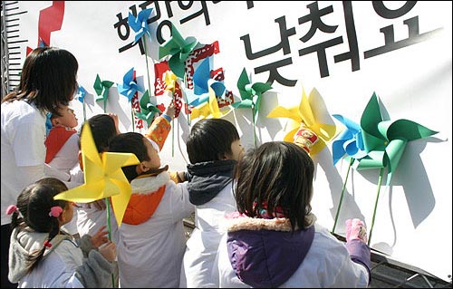 바람개비를 현수막 위에 붙이고 있는 아이들. 